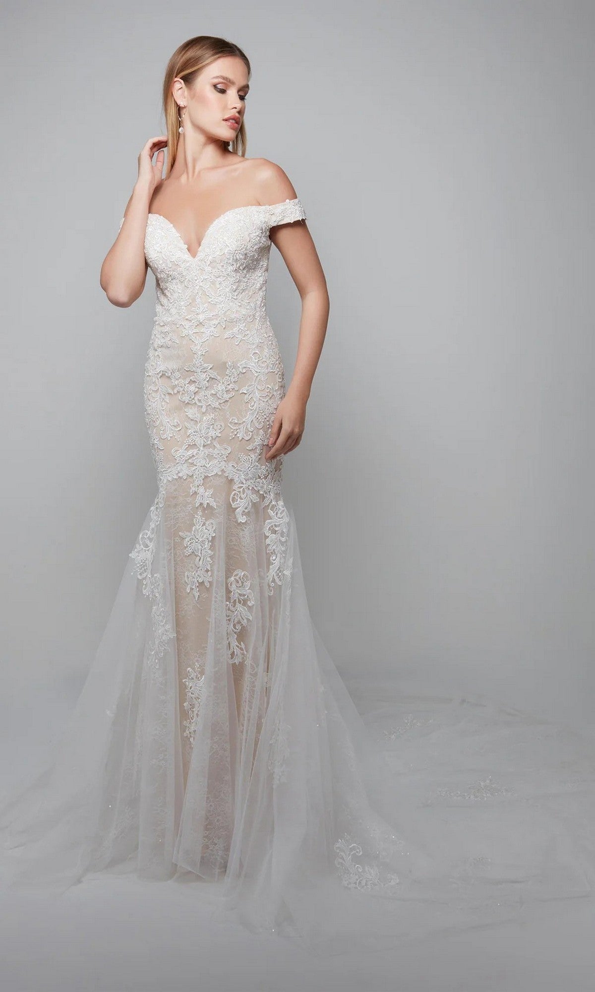 A woman in the Alyce 7086 long ivory dress with floral lace appliques and a sheer tulle skirt stands against a plain gray background.